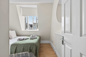 A bedroom with a bed, a window, a radiator, and a door. - South Ken 2-Bed - Science Museum - Lift - Sleeps 6 (London)