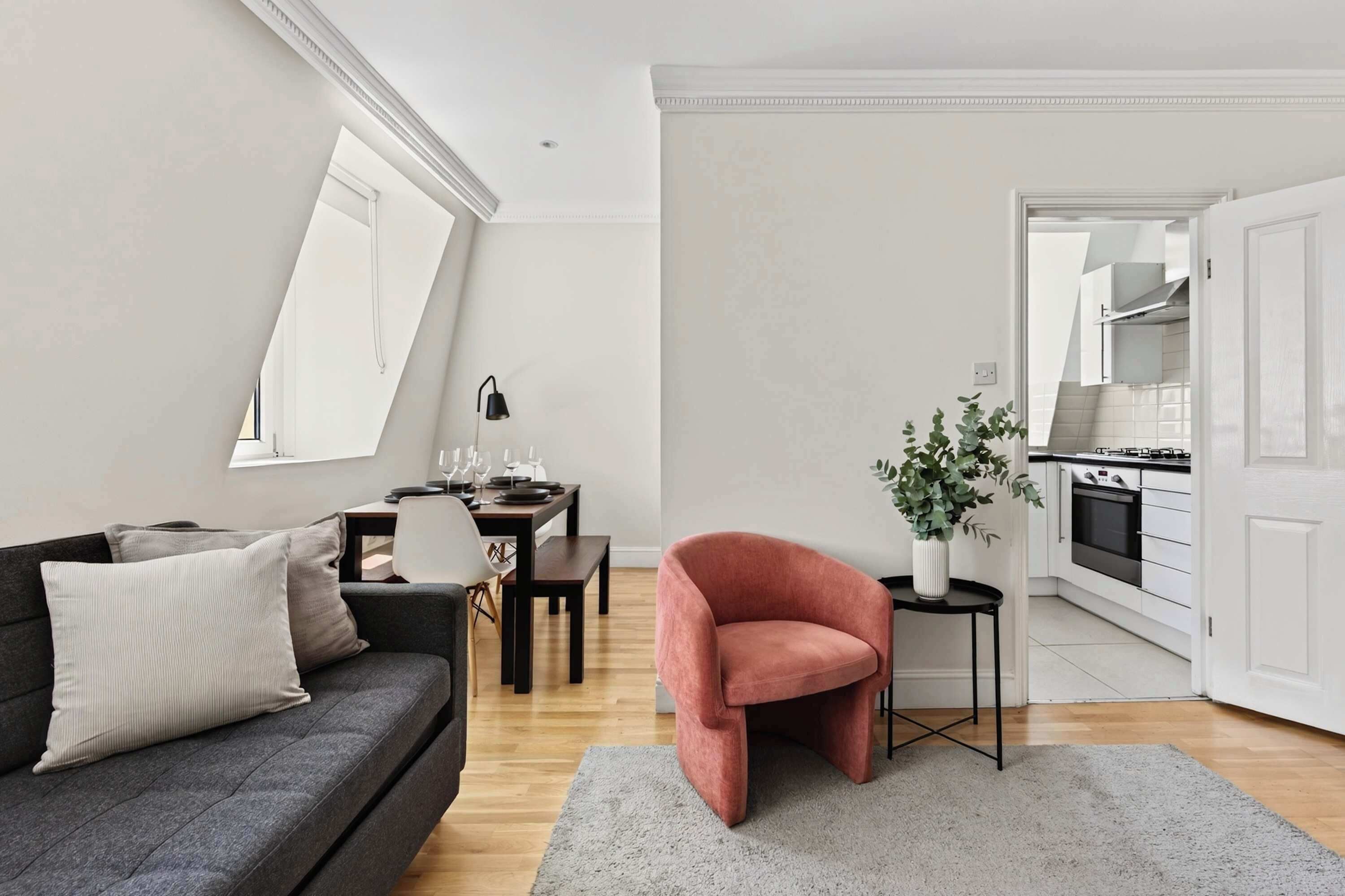 Ett modernt vardagsrum med en soffa, ett matbord för fyra personer och ett kök som syns genom en öppen dörr.