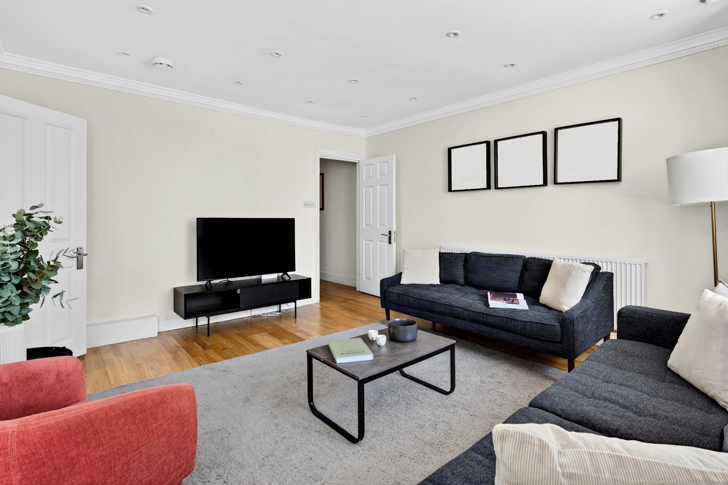 A modern living room with a flat-screen TV, a dark sofa, a red armchair, a coffee table, and a floor lamp.
