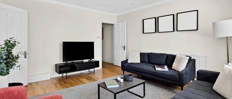 Una sala de estar moderna con un televisor de pantalla plana, un sofá oscuro, un sillón rojo, una mesa de centro y una lámpara de pie.