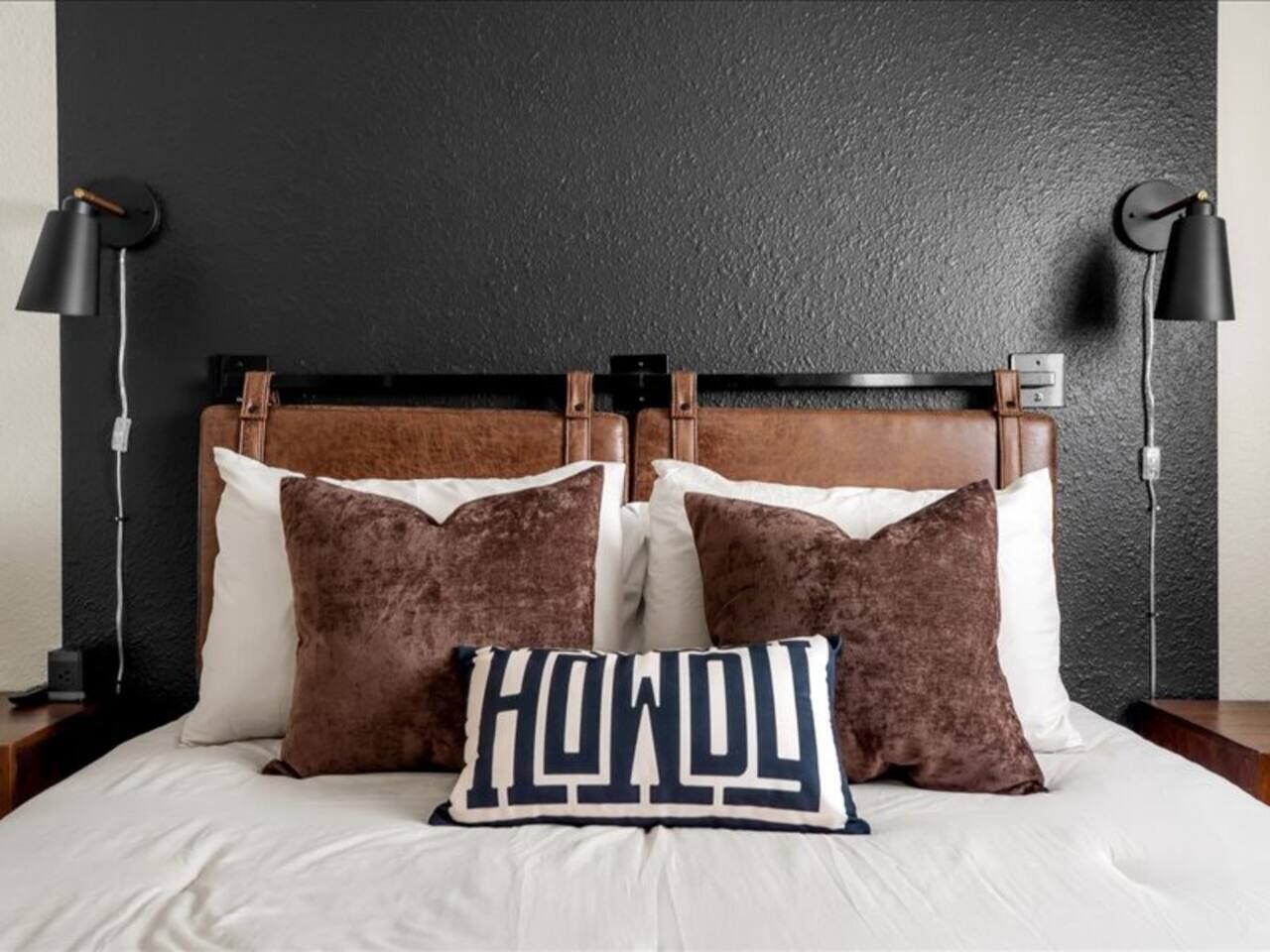 A bed with a headboard, two bedside lamps, and a pillow with the word 'Hawaii' on it.