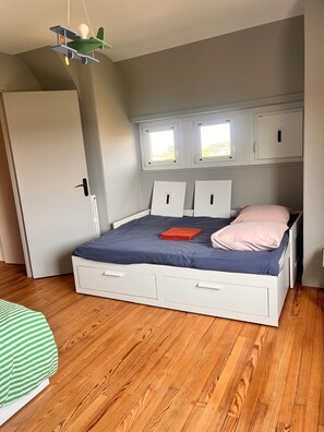 Ein Schlafzimmer mit einem Bett, zwei Fenstern, einem Kleiderschrank und einer Pendelleuchte.