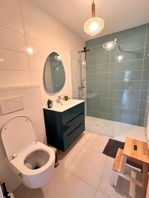 Ein modernes Badezimmer mit Toilette, Waschtisch, Spiegel, Dusche und einem kleinen Holzschemel.