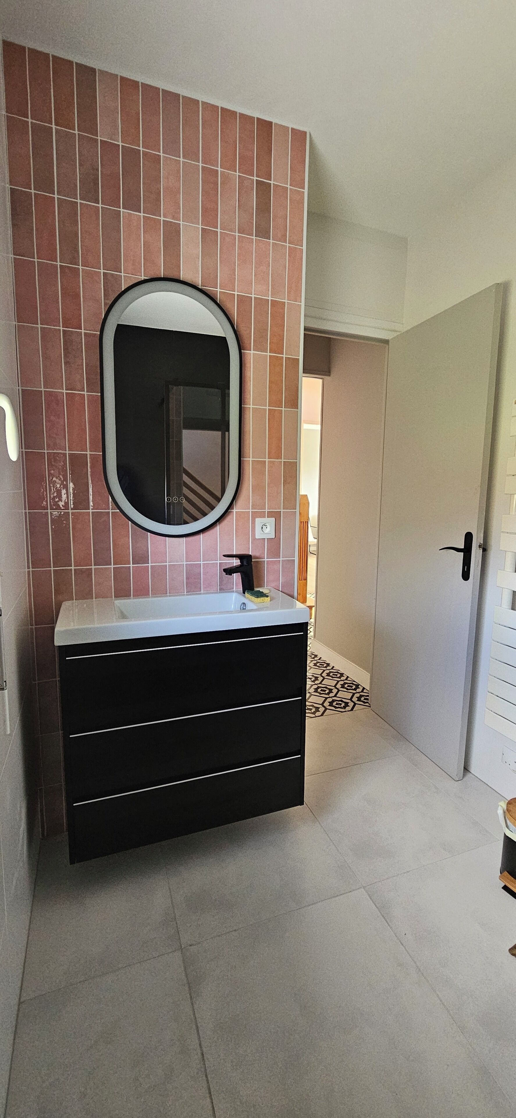 A bathroom with a large mirror, a black vanity, and a tiled floor.