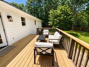 Eine Terrasse mit Gartenmöbeln, einem Holzgeländer und einem weißen Haus im Hintergrund.