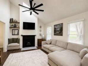 A living room with a fireplace, a sofa, a television, and a ceiling fan.