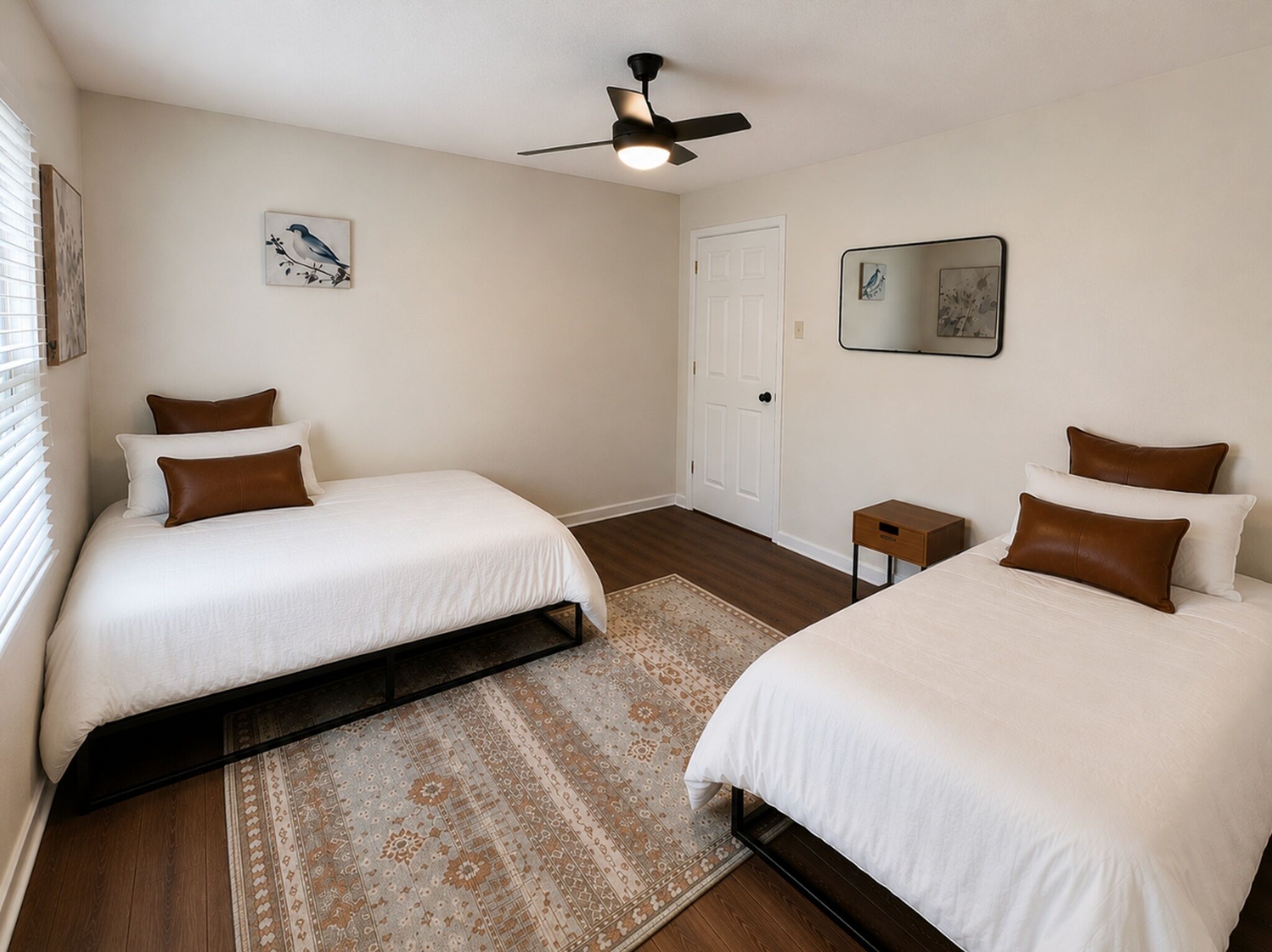 Ein Hotelzimmer mit zwei Betten, einem Deckenventilator, einer Tür und einem kleinen Nachttisch.