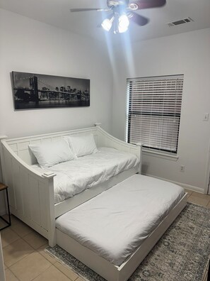 Ein Schlafzimmer mit einem weißen Bett, einem Deckenventilator, einem Fenster mit Jalousien und einem Stadtbild an der Wand.