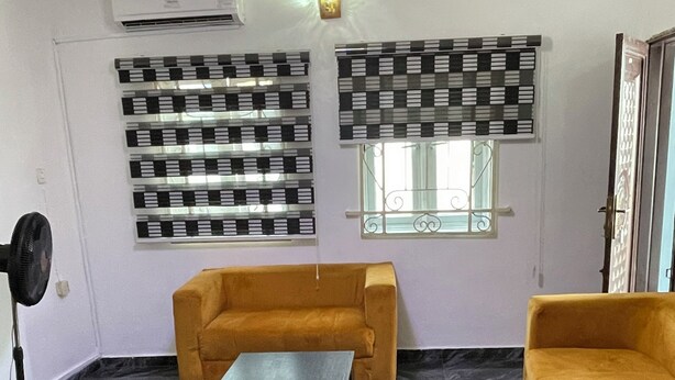 Una habitación con sofá, mesa de centro, ventilador y ventana con persianas decorativas.