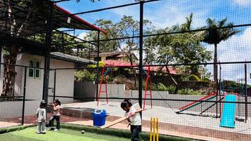 Zona de entrenamiento de críquet al aire libre con una valla de malla, un jaulón para bateadores y un pequeño pabellón.
