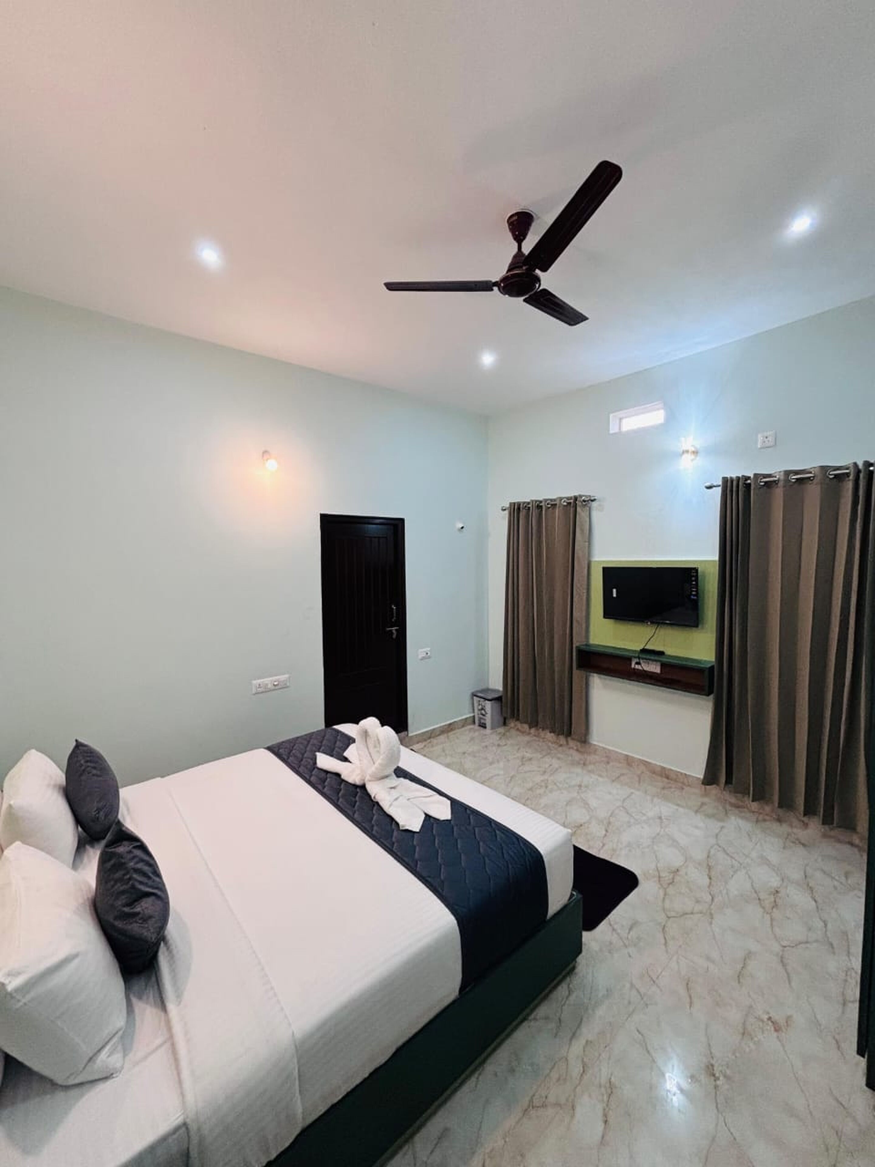 Una habitación de hotel con una cama, ventilador de techo, televisor y cortinas.