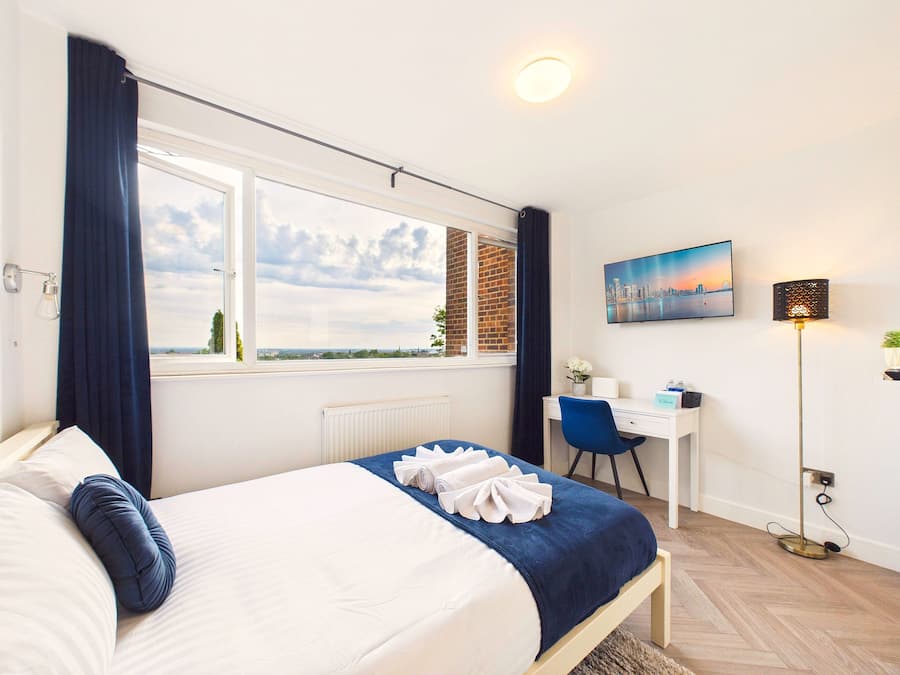 A hotel room with a bed, a desk, a chair, a lamp, and a painting on the wall.