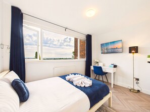 Habitación de hotel con cama, escritorio, silla, lámpara y un cuadro en la pared.