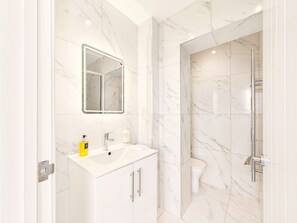 Un baño con lavamanos blanco, espejo y azulejos de mármol.
