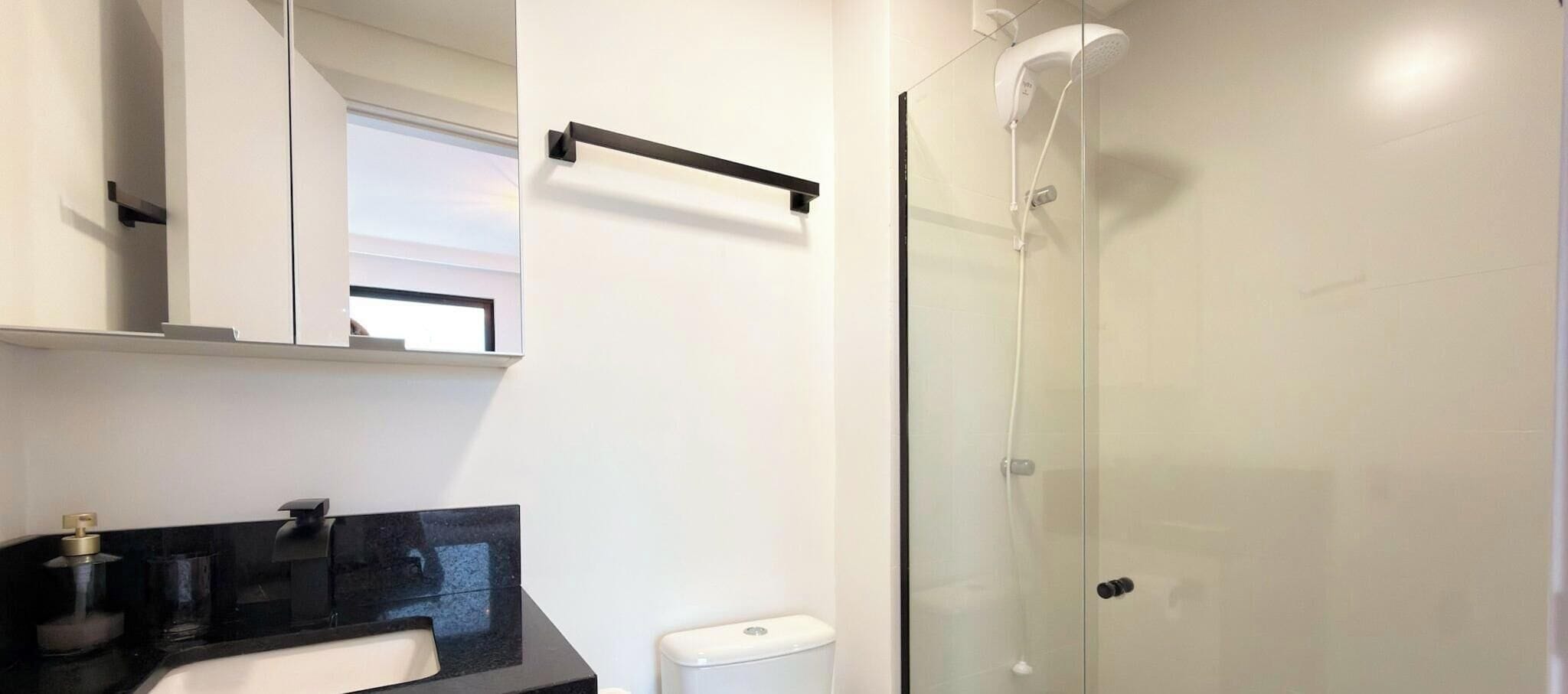 Un baño con cabina de ducha de vidrio, encimera negra y inodoro blanco.