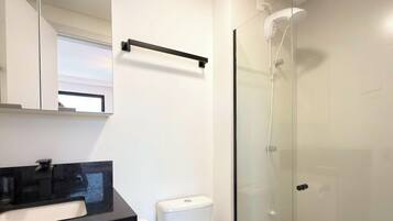 Un baño con cabina de ducha de vidrio, encimera negra y inodoro blanco.