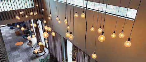 A modern interior with hanging light bulbs, a seating area with a sofa and chairs, and a view through a window.
