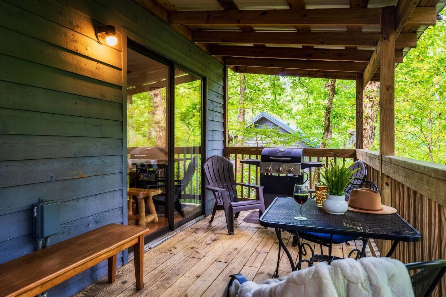 A covered outdoor deck with a grill, seating, and a view of the surrounding greenery.