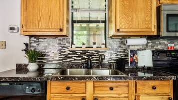 A kitchen with wooden cabinets, a stainless steel sink, a window with blinds, and a backsplash with black and white tiles.