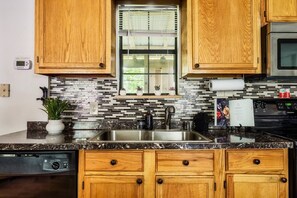 A kitchen with wooden cabinets, a stainless steel sink, a window with blinds, and a backsplash with black and white tiles.