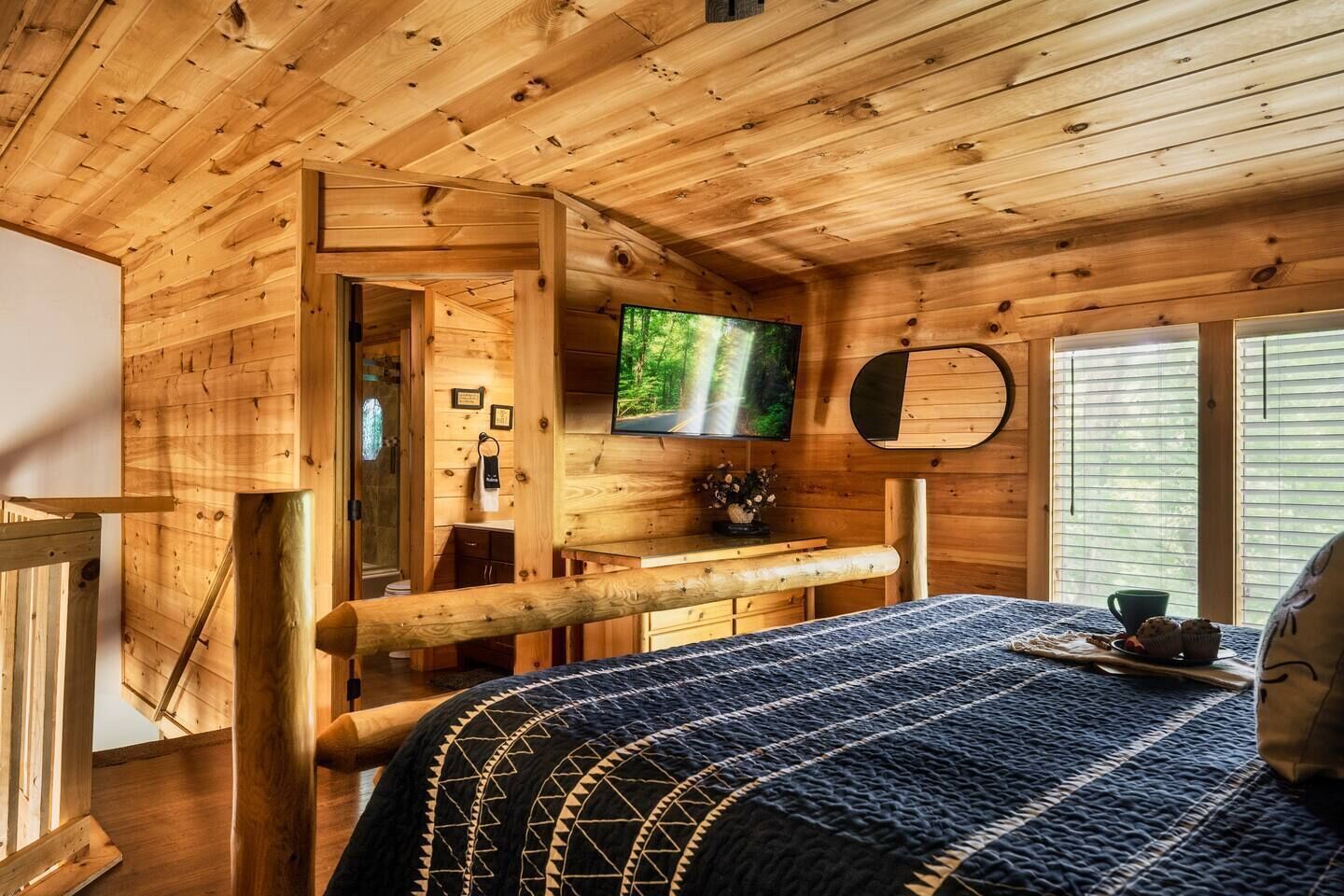 L’intérieur d’un chalet en bois, avec un lit, un téléviseur et une fenêtre équipée de stores.