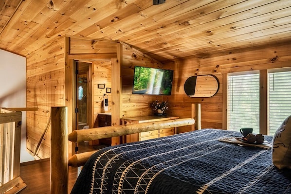 L’intérieur d’un chalet en bois, avec un lit, un téléviseur et une fenêtre équipée de stores.