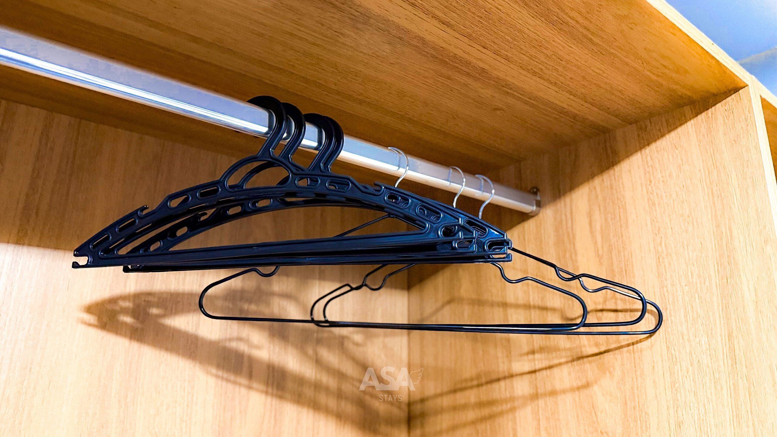 A wooden closet with a metal rod and two black hangers.