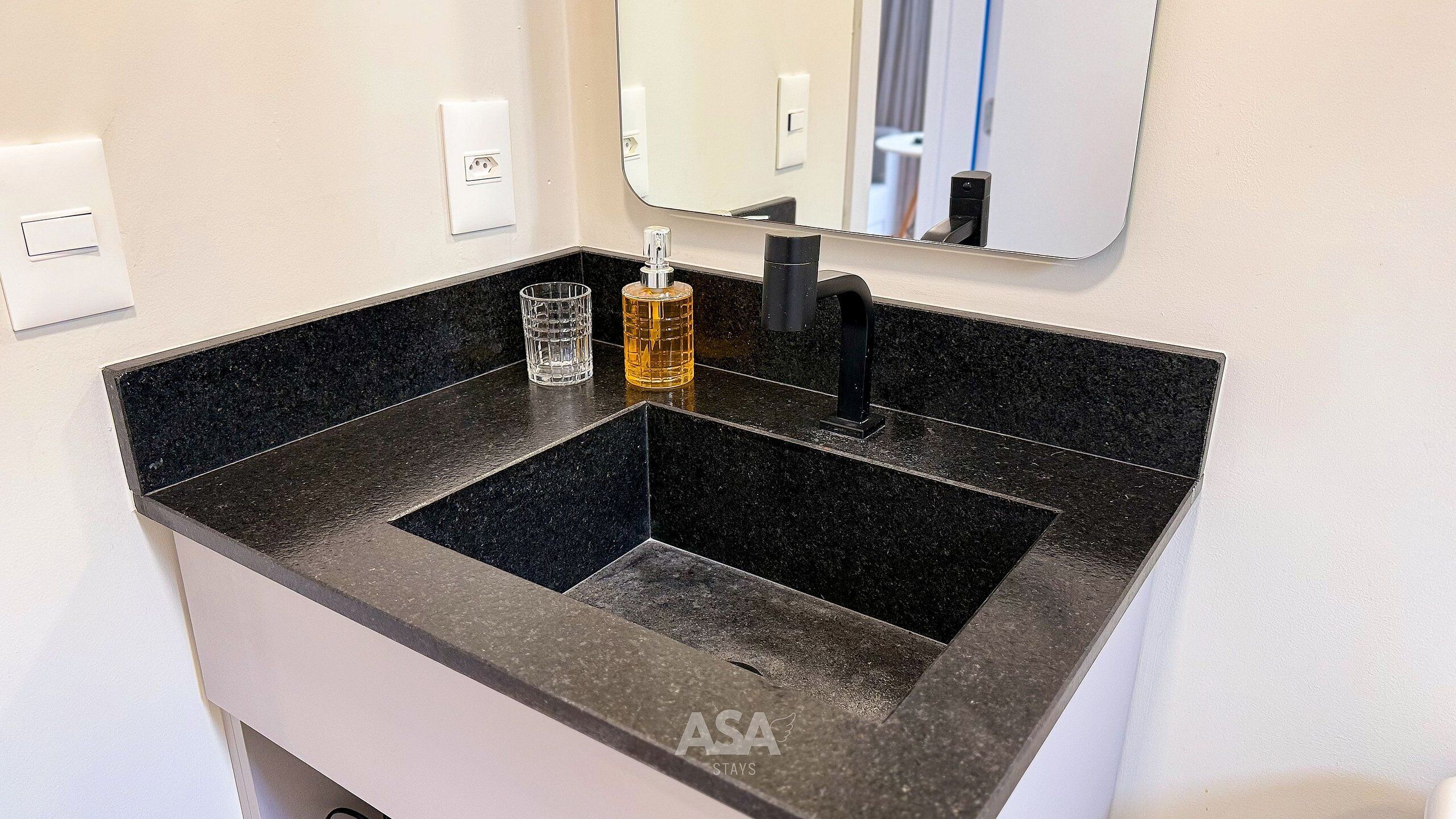 A bathroom with a black granite sink, a glass, and a bottle of hand soap.