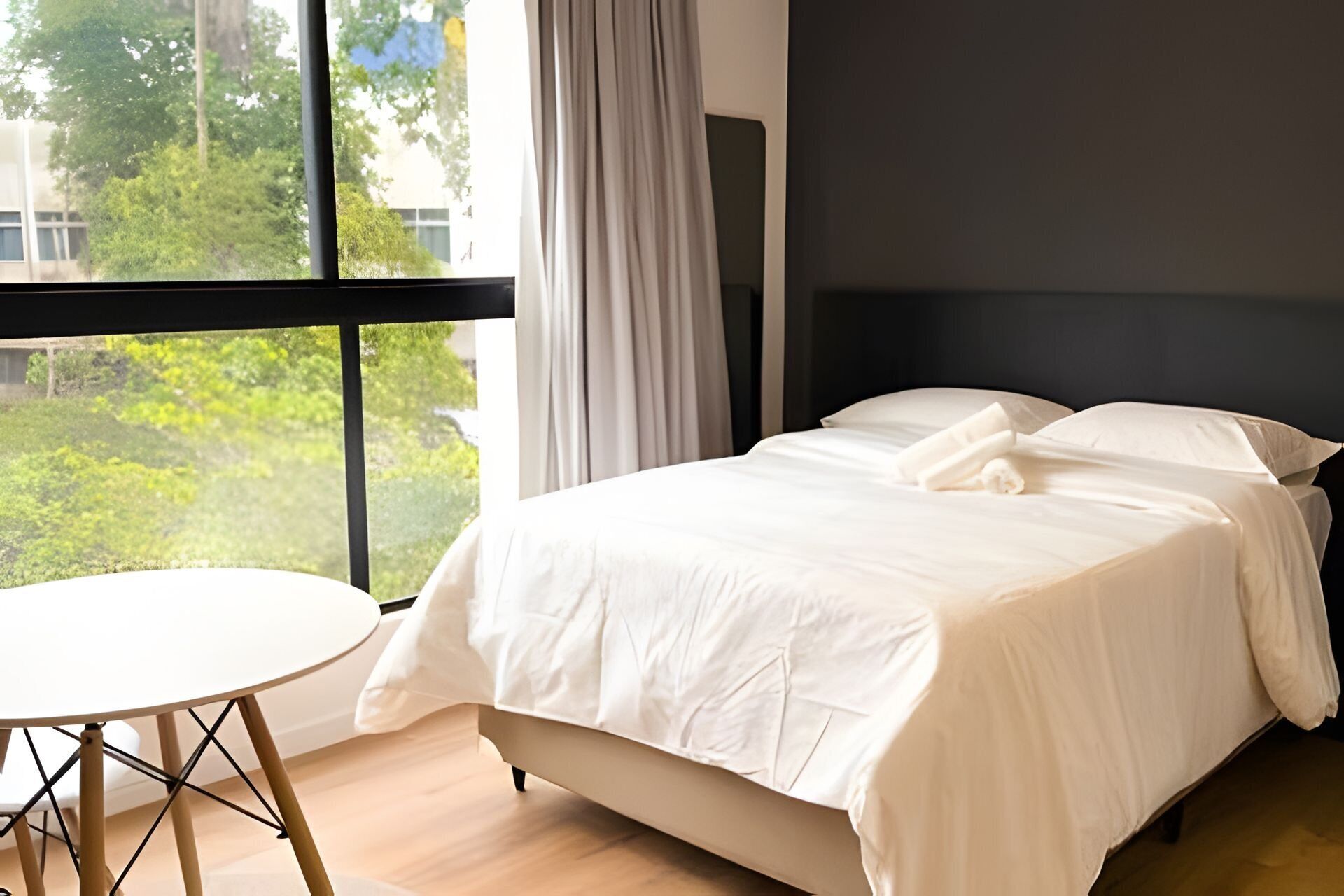 Un dormitorio con una cama, una mesa redonda y vistas al verdor exterior.
