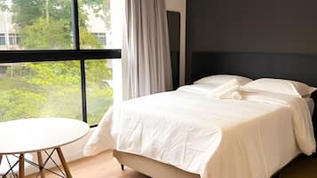Un dormitorio con una cama, una mesa redonda y vistas al verdor exterior.