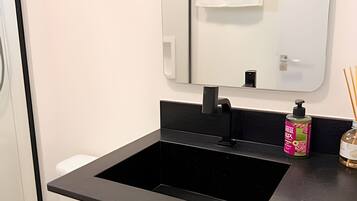 A bathroom with a black sink, a mirror, and a bottle of hand soap on the counter.