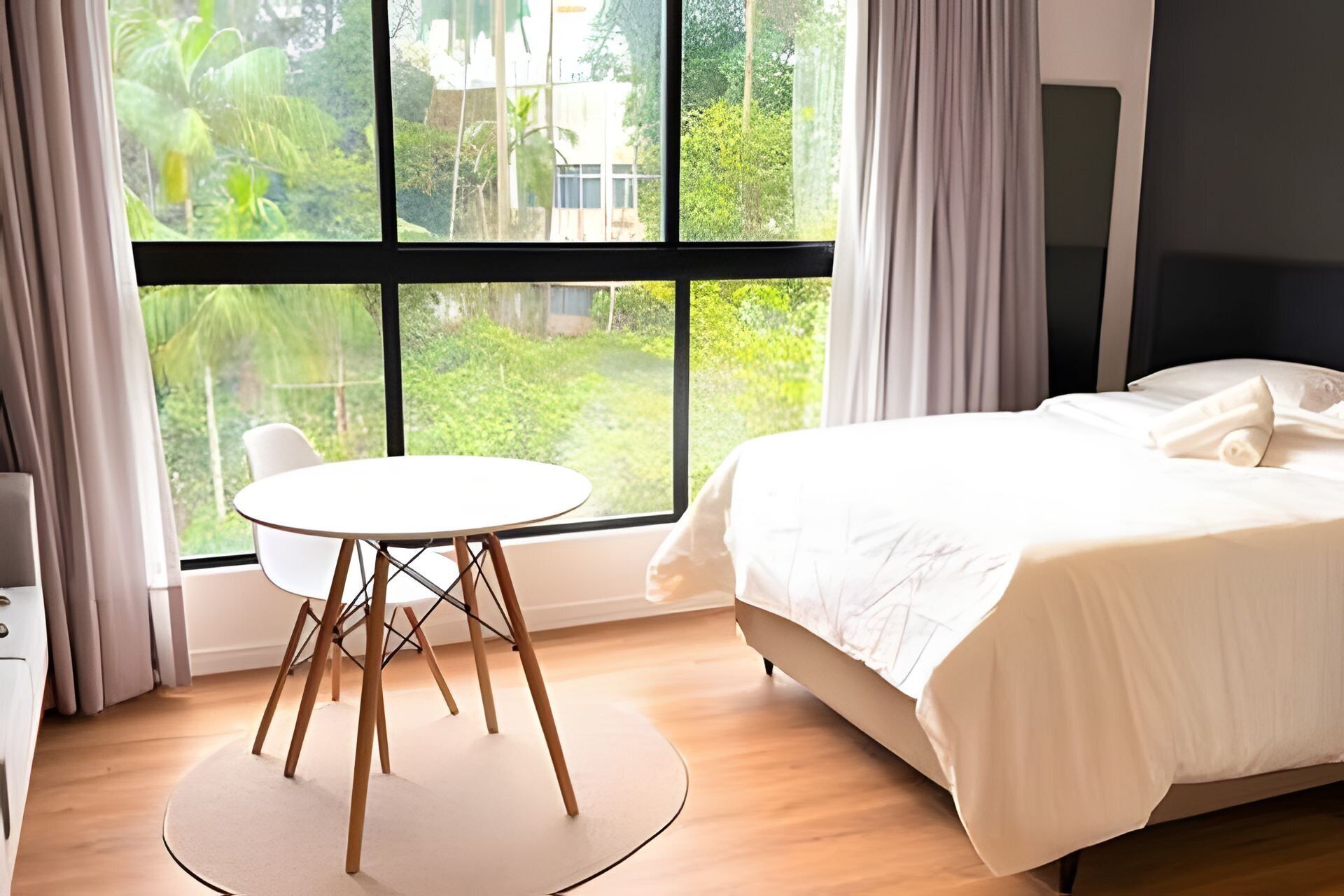 Una habitación de hotel con una cama, una mesa redonda y vista a áreas verdes.