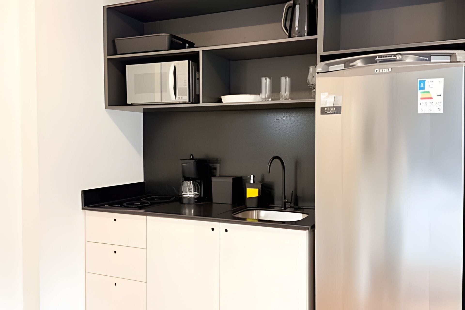 Cocina compacta con microondas, cafetera y refrigerador de acero inoxidable.