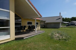 A house with a covered patio, a fenced yard, and a car parked nearby.