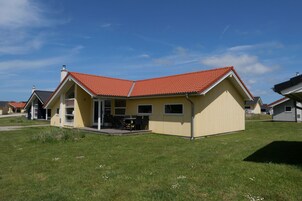 A yellow house with a red roof, a patio with chairs, and a clear blue sky.