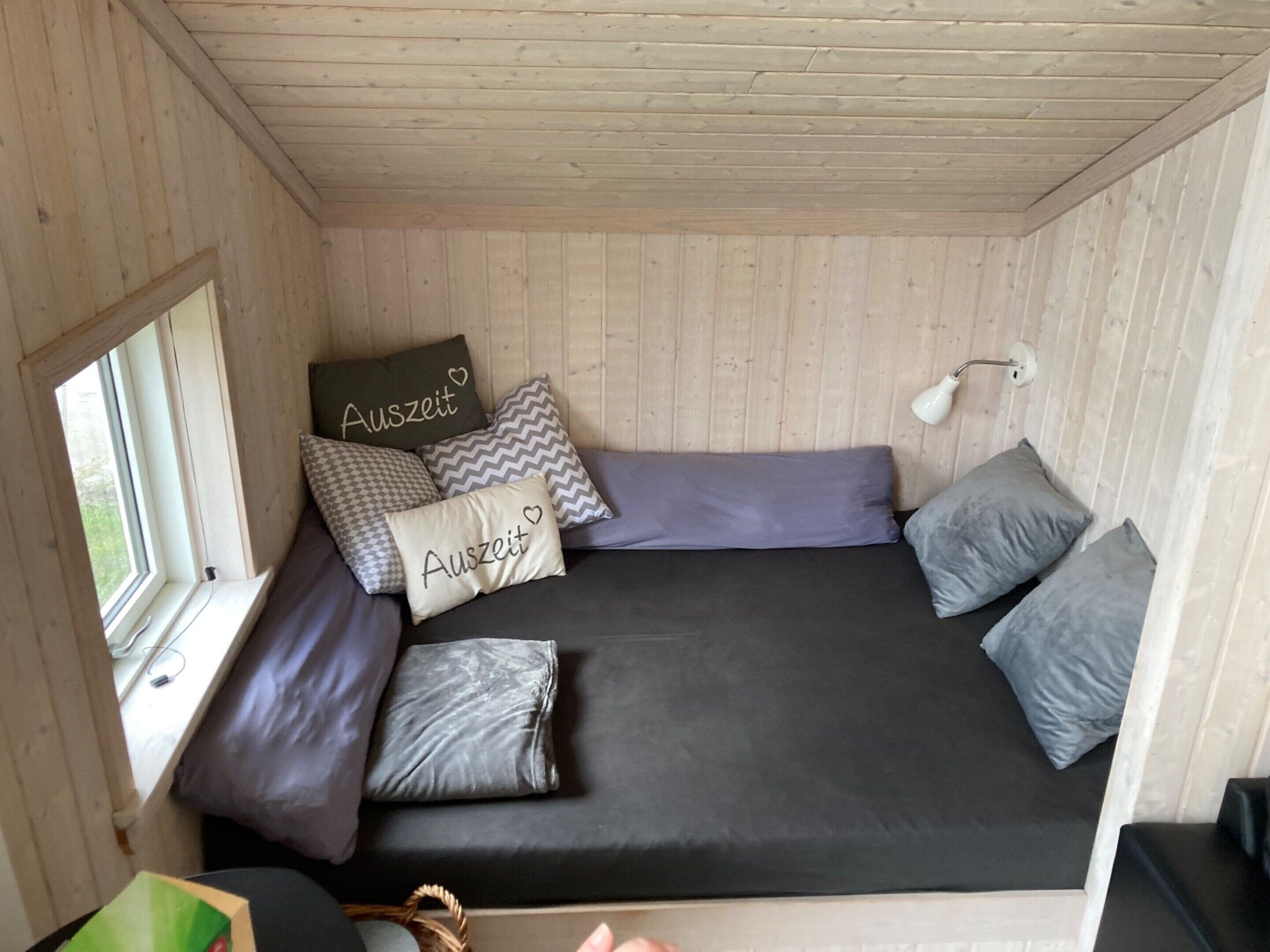 A compact room with a bed, pillows, a window, and a lamp.