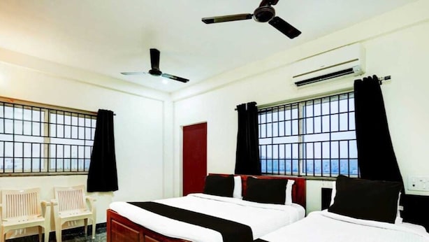 A hotel room with two beds, a ceiling fan, an air conditioning unit, and a window with bars. - Deluxe Cochin Apartments Annex (Aluva)