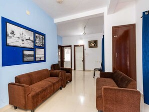 A room with two brown sofas, a white ceiling, and a blue wall with framed pictures. - Deluxe Cochin Apartments Annex (Aluva)