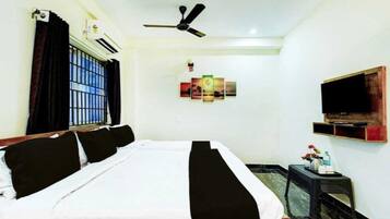 A hotel room with a bed, a ceiling fan, a mounted TV, and a window with bars.
