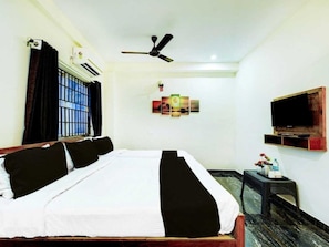 A hotel room with a bed, a ceiling fan, a mounted TV, and a window with bars. - Deluxe Cochin Apartments Annex (Aluva)