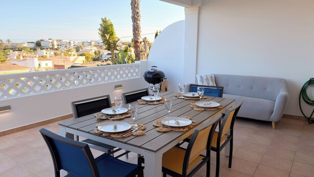 Un área de comedor al aire libre con una mesa para cuatro, una parrilla y un sofá.