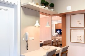 A modern dining area with a white table, chairs, pendant lights, and a visible phone on the wall.