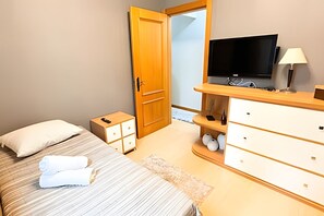 A bedroom with a bed, a bedside table with a lamp, a TV, and a wardrobe.