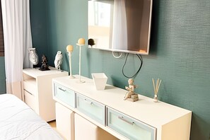 A bedroom with a bed, a white dresser with drawers, a television mounted on the wall, and a decorative bird statue. - ASA Apto Vale Dourado Frente-mar Hidro 2vgs (Balneário Camboriú)