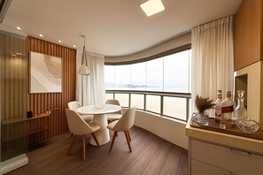 Un comedor moderno con una mesa redonda y sillas, vista al mar a través de ventanas amplias, y una obra de arte colgada en la pared.
