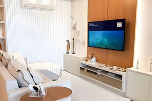 Ein modernes Wohnzimmer mit einem Flachbildfernseher an einer Holzwand, einem weißen Sofa und einem kleinen Couchtisch.