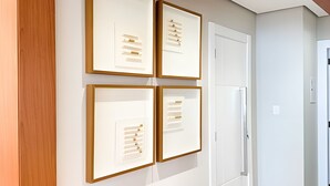 A hallway with four framed artworks on the wall, a white door, and a white cabinet. - ASA Apto Vale Dourado Frente-mar Hidro 2vgs (Balneário Camboriú)