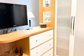 A room with a flat-screen TV, a lamp, a small table, and a cabinet with drawers. - ASA Apto Vale Dourado Frente-mar Hidro 2vgs (Balneário Camboriú)