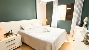 A neatly arranged bedroom with a bed, bedside tables, a lamp, and a decorative item. - ASA Apto Vale Dourado Frente-mar Hidro 2vgs (Balneário Camboriú)