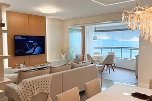 Ein modernes Wohnzimmer mit großem Flachbildfernseher, einer Couch, einem Esstisch und einem Balkon mit Blick.